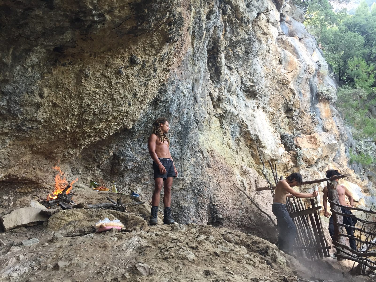 A simple camp under a rock overhang — fire, cliff face, the ground found before dark